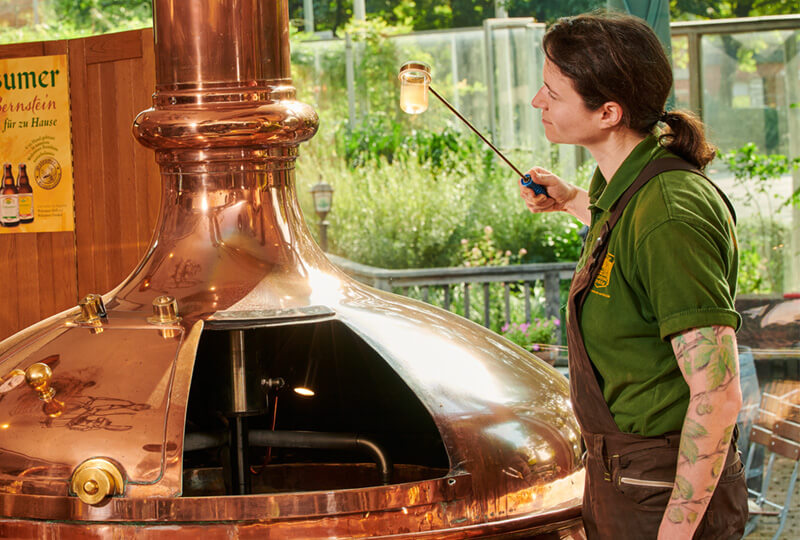 Braumeisterin entnimmt Bierprobe aus einem großen Kessel